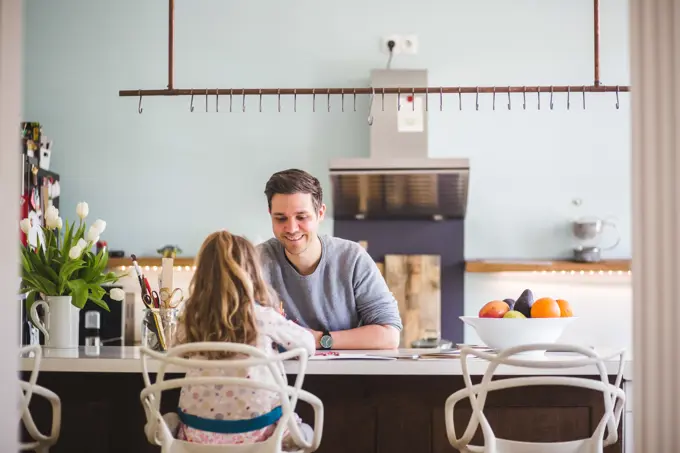 Happy father assisting daughter studying in kitchen at home