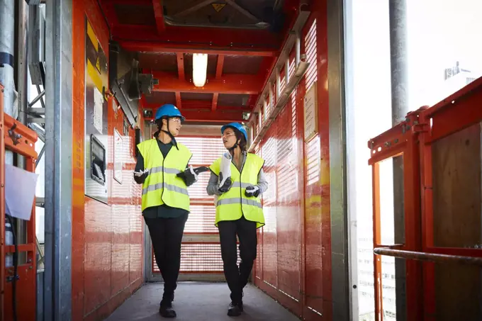 Full length of female engineers discussing while walking in freight elevator at construction site