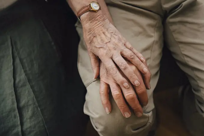 Midsection of retired senior couple holding hands sitting at nursing home