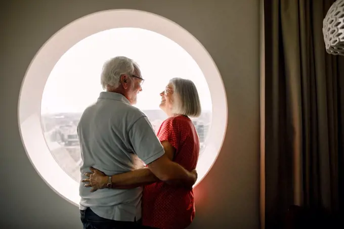 Senior couple embracing while standing by window in hotel room