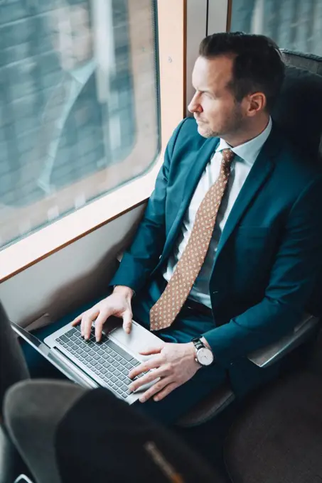 High angle view of businessman using laptop while looking through train window