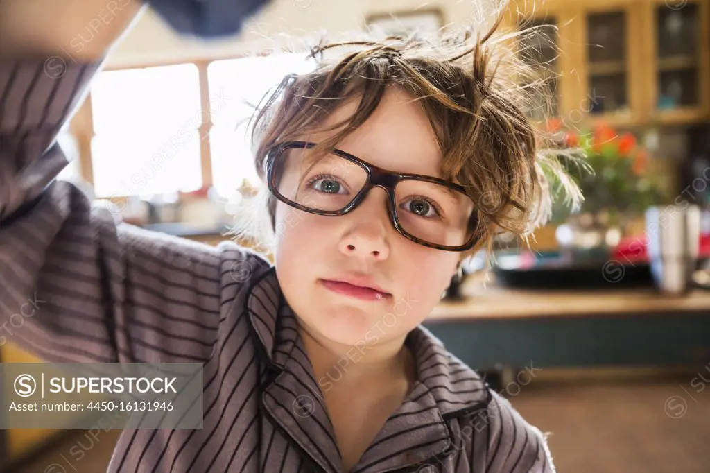 Portrait of a six year old boy with disheveled hair and oversized glasses  waking up. Bedhead hair. - SuperStock