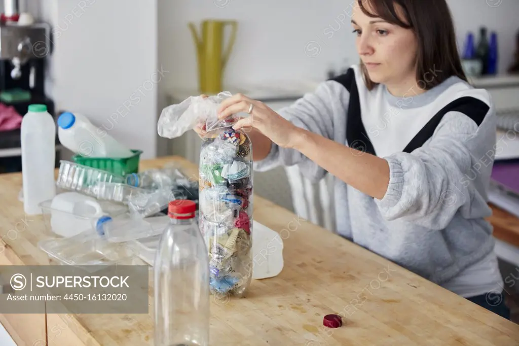 Woman stuffing soft waste plastics into large plastic bottle to make an ecobrick for use as a  building block