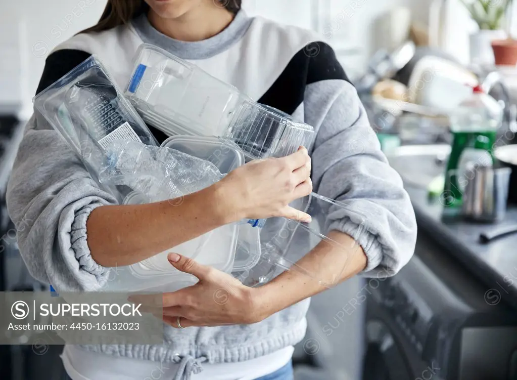 Woman holding armful of used plastic containers in kitchen
