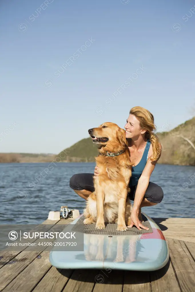 A woman and a retriever dog on a paddleboard on the jetty.