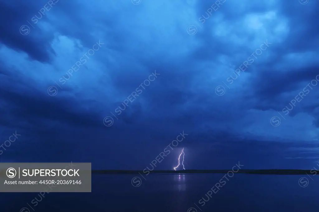 A lightning strike reflected in the water of a lake. Dark stormy dramatic sky.