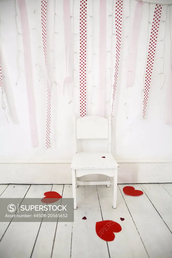 Empty chair in a photographers studio, fairy lights and red streamers on  the wall, heart-shaped paper cut-outs on the white wooden floor. -  SuperStock