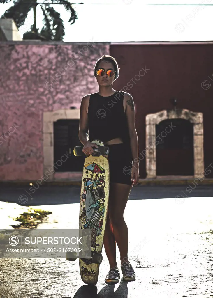 Young woman holding a skateboard and standing in the street.