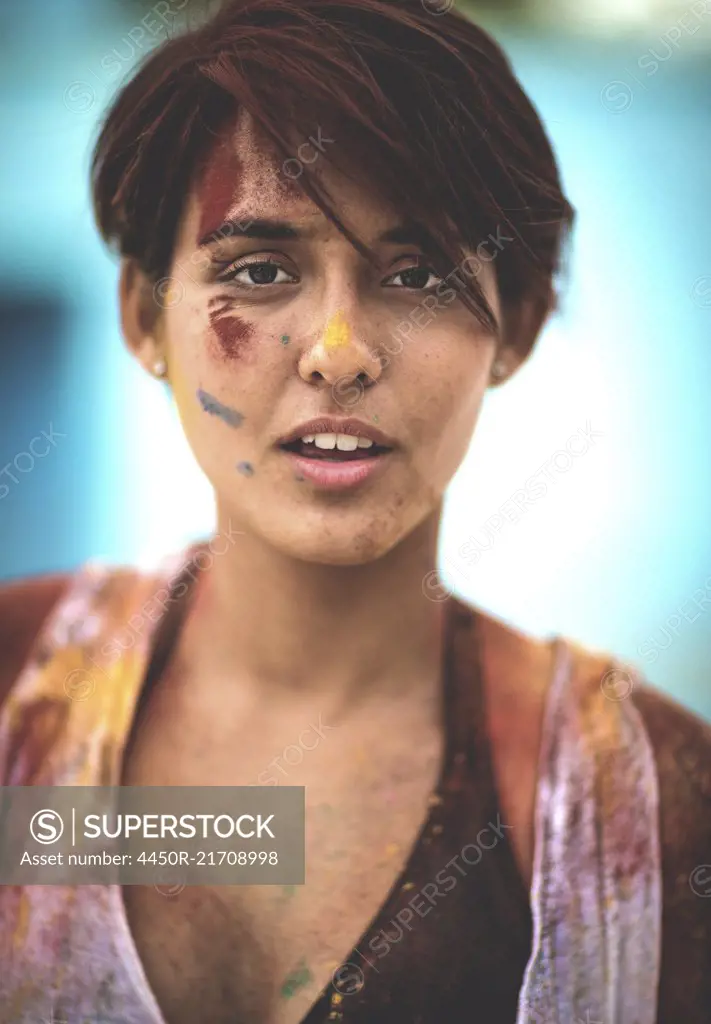 Young woman covered in paint looking into camera.