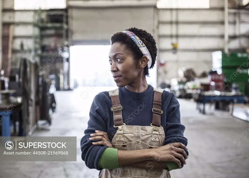 Black woman factory worker wearing coveralls in a large sheet metal factory.