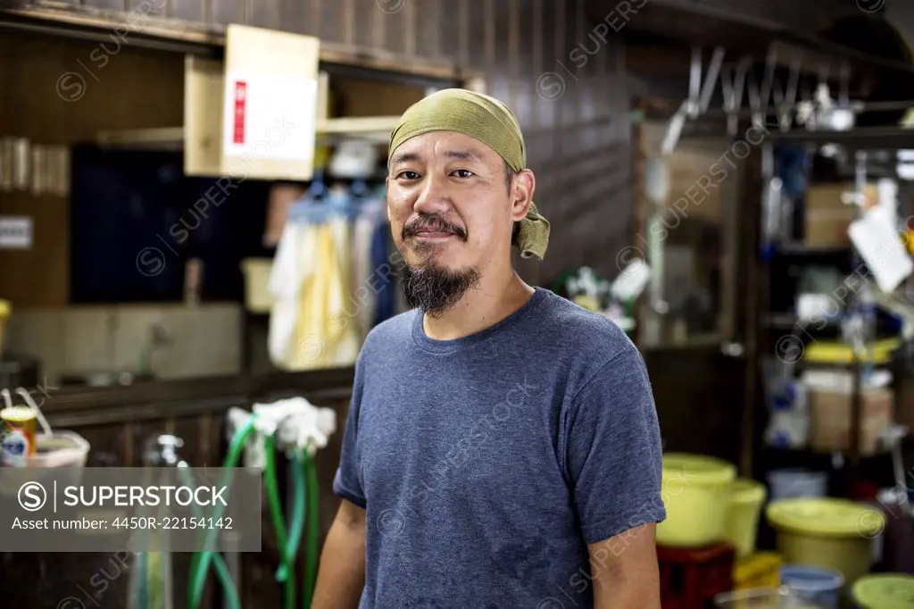 Japanese man wearing bandana in a textile dyeing workshop, smiling at camera.