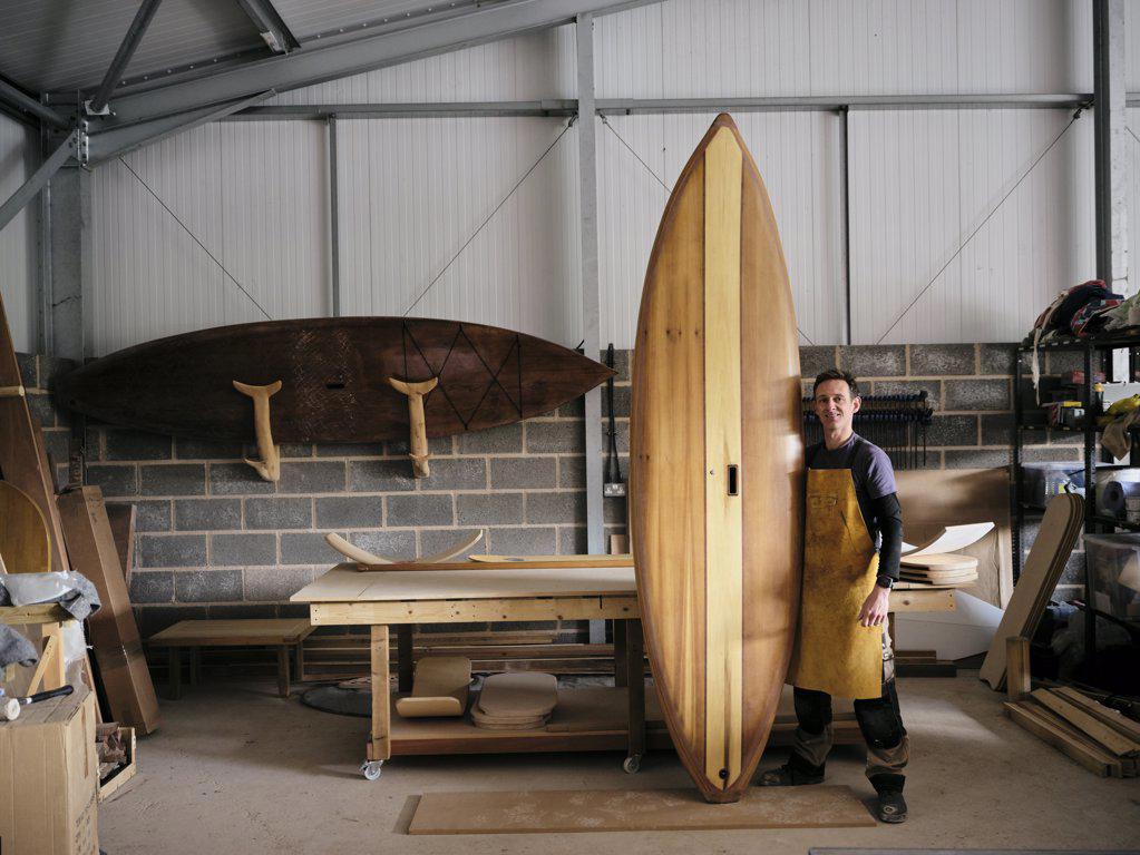 Portrait of man holding hand made wooden paddleboard in workshop
