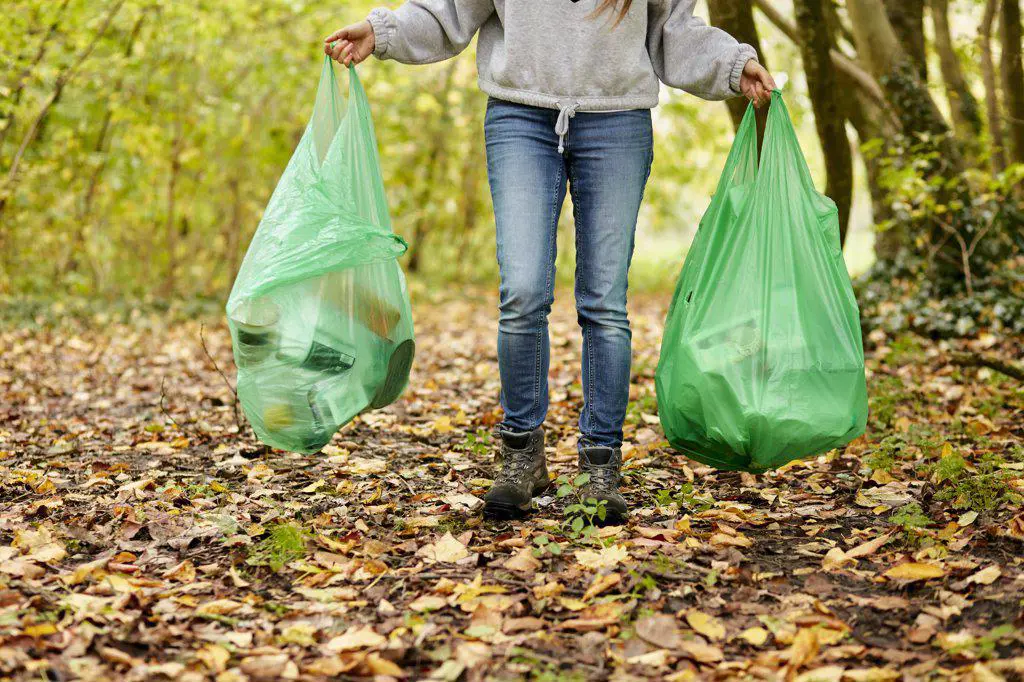 Woman walking in woodland holding two plastic bags full of rubbish
