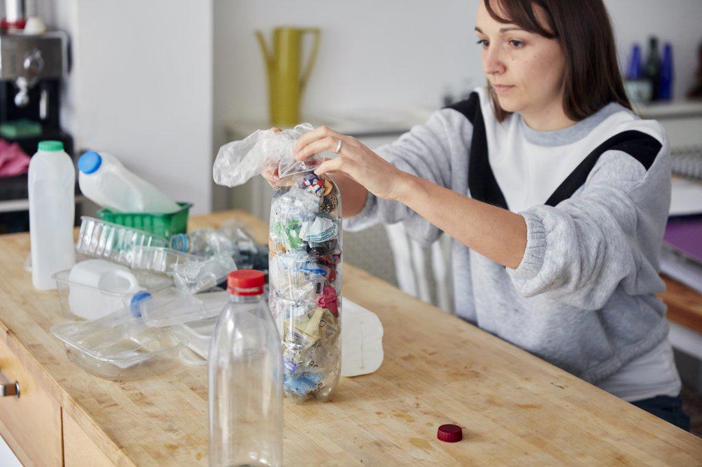 Woman stuffing soft waste plastics into large plastic bottle to make an ecobrick for use as a  building block