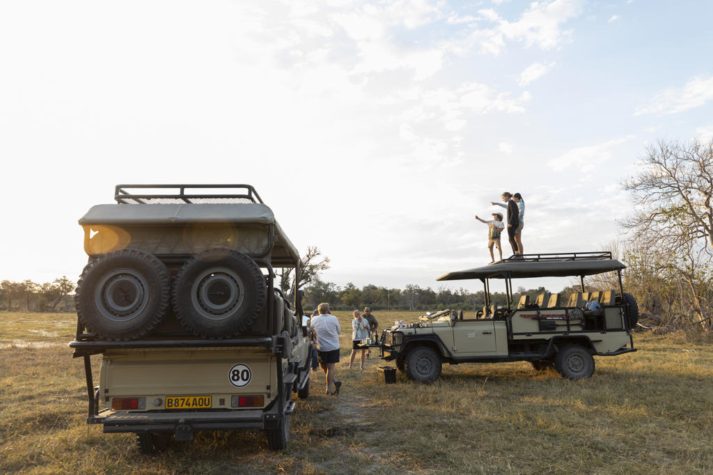 Group of people standing around safari vehicles on an early morning game drive