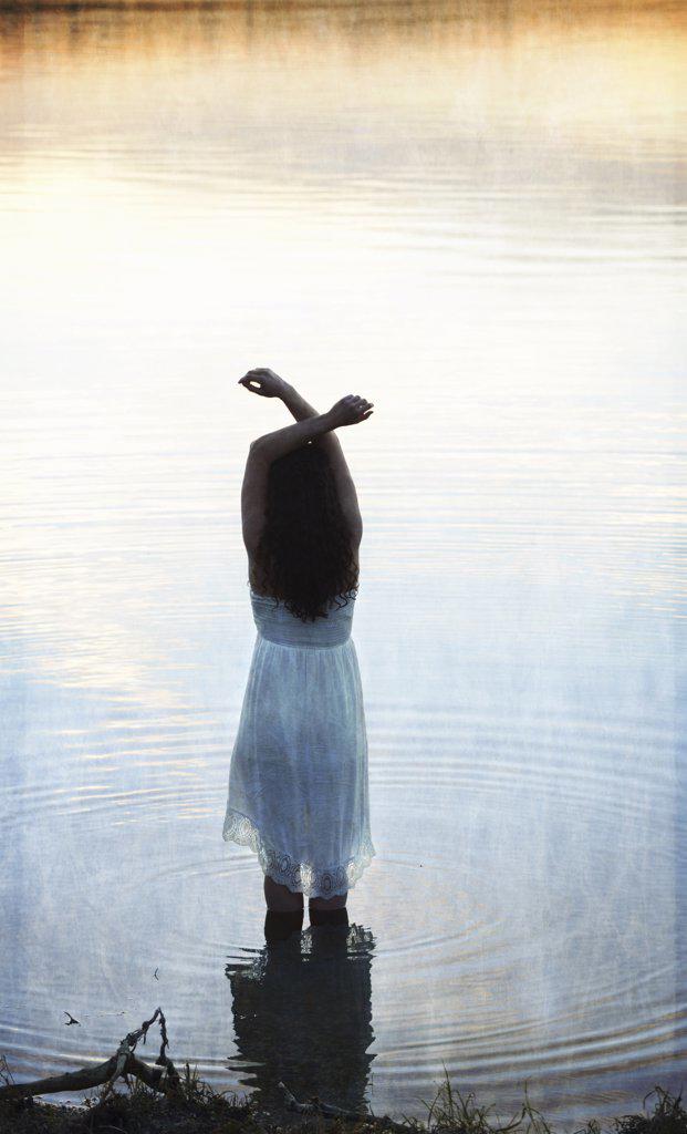 A woman in a white dress in shallow water at dusk