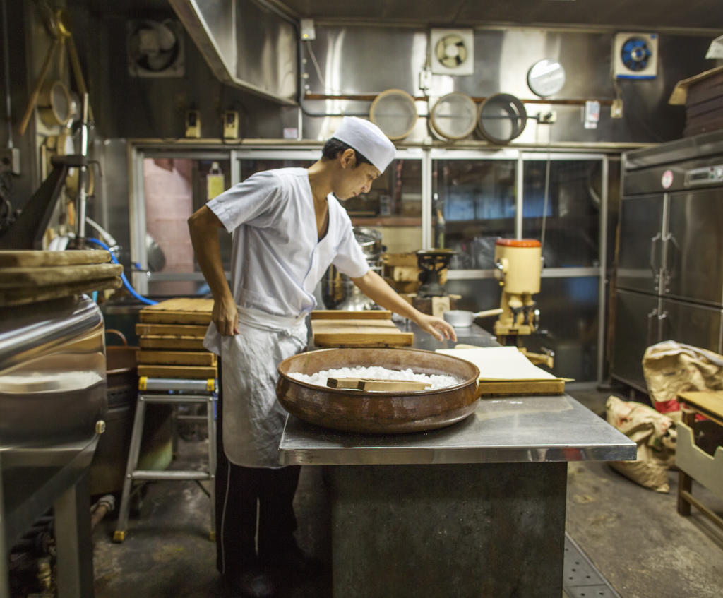 A small artisan producer of wagashi. A man mixing a large bowl of ingredients and pressing the mixed dough into moulds in a commercial kitchen.