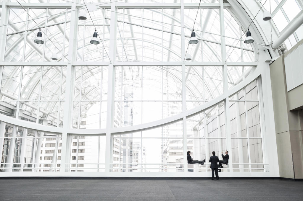 Three businesspeople meeting in front of a window in a large convention center loggy.