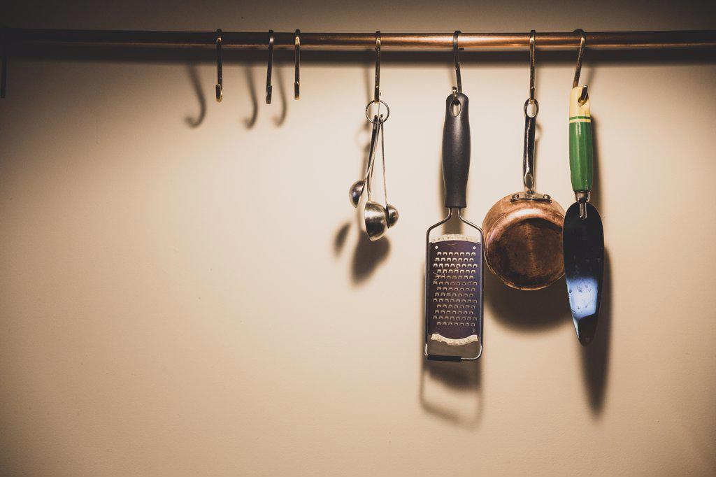 Close up of kitchen utensils suspended from copper pipe.