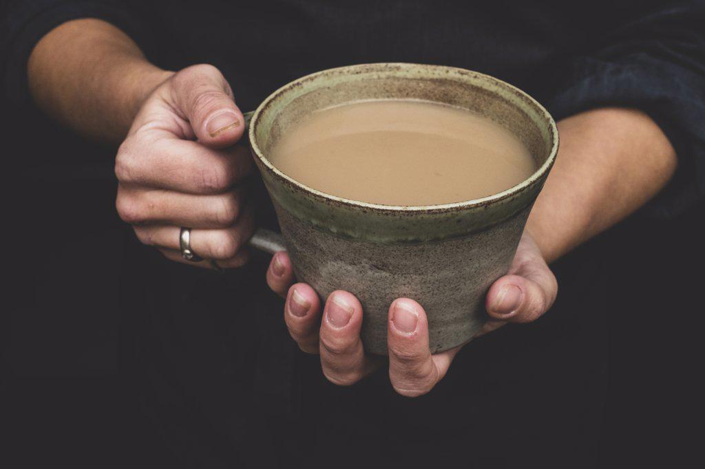 High angle close up of human hands holding green earthenware mug of tea.