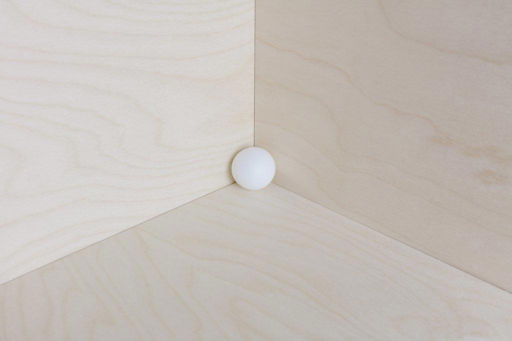Single white ball in corner of a wooden box.