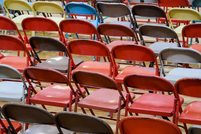 Rows of metal folding chairs of different colours, grey, red, yellow. 