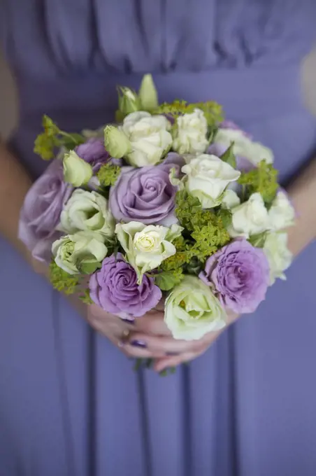 A bridesmaid in a blue dress holding a bouquet of pink and white roses.