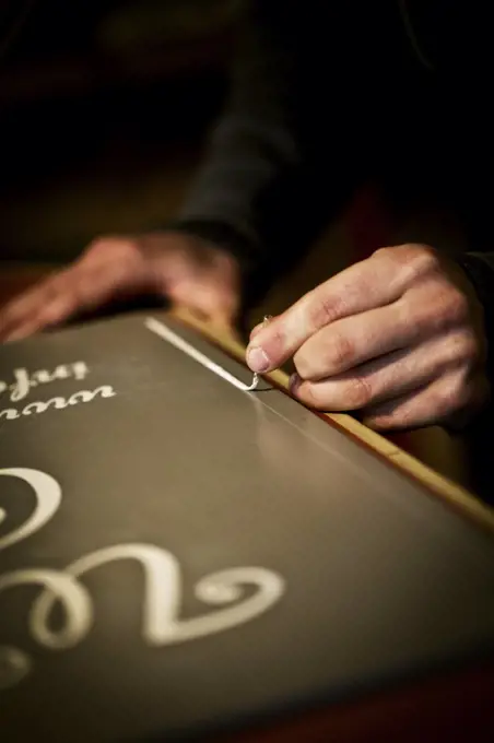 A signwriter working with a loaded brush painting a line freehand on the edge of a sign.