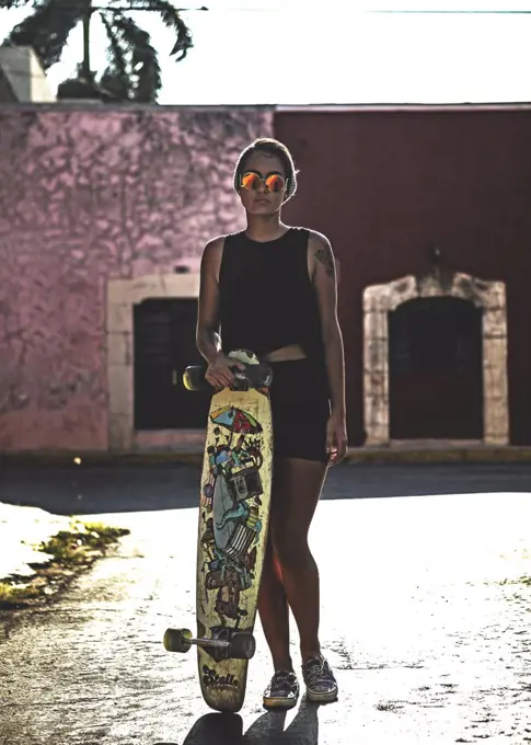 Young woman holding a skateboard and standing in the street.