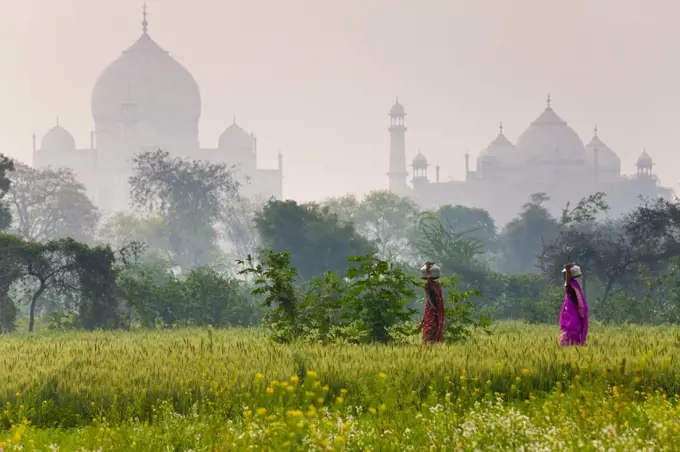 Exterior view of the Taj Mahal in Agra, India. Two woman in the foreground carrying loads on their heads.