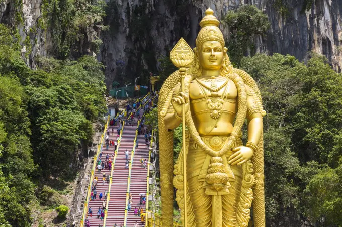Colossal golden statue of Hindu deity, with stairway into cave in the background.