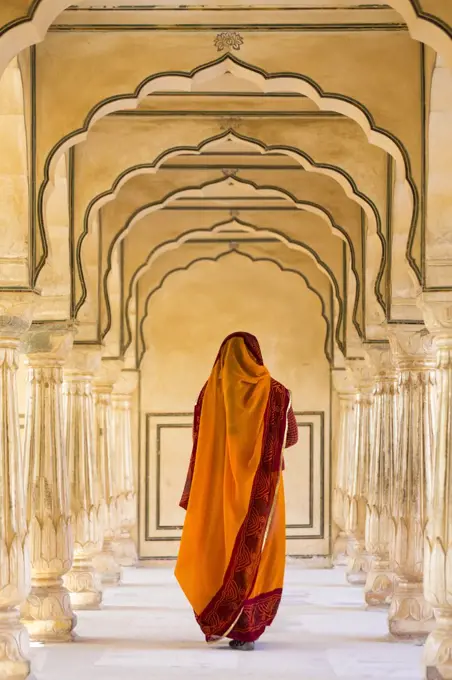 Rear view of woman wearing orange sari walking along a colonnade.
