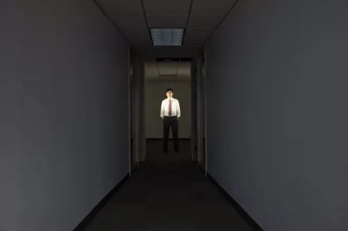 A portrait of a black businessman standing at the end of a long dark hallway.