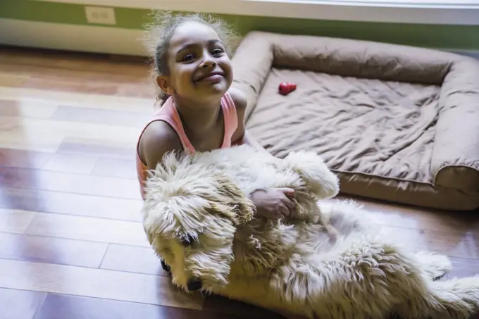 Smiling girl sitting on floor hugging labradoodle puppy