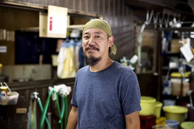 Japanese man wearing bandana in a textile dyeing workshop, smiling at camera.
