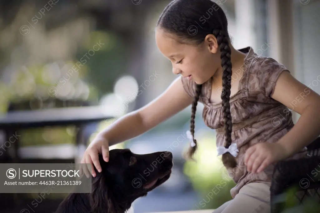 Young girl patting a dog on a porch.