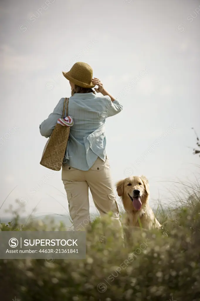 Mid-adult woman standing with a dog on grassy dunes of a beach.