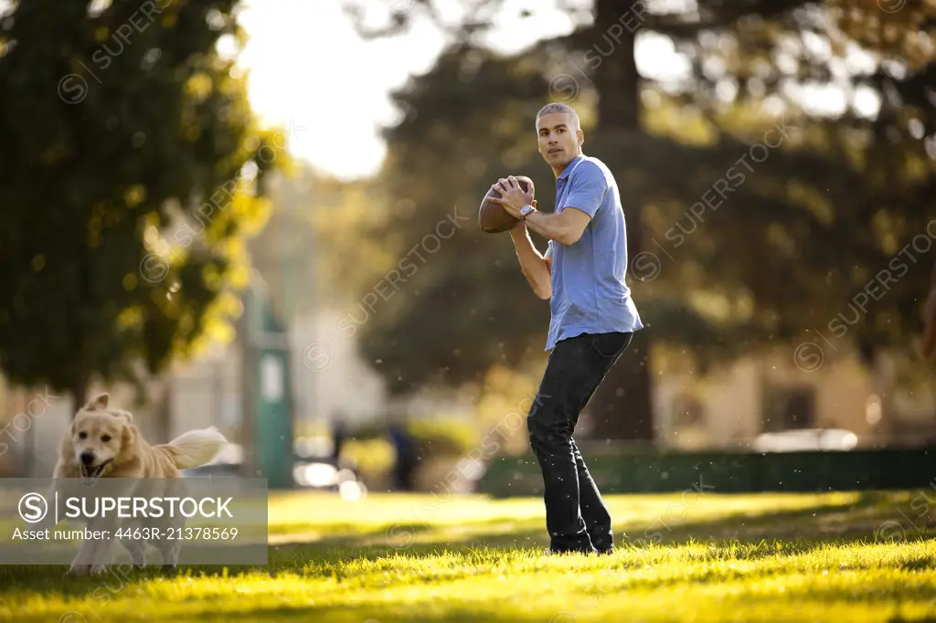 Mature man preparing to throw a football while in the park with his dog.