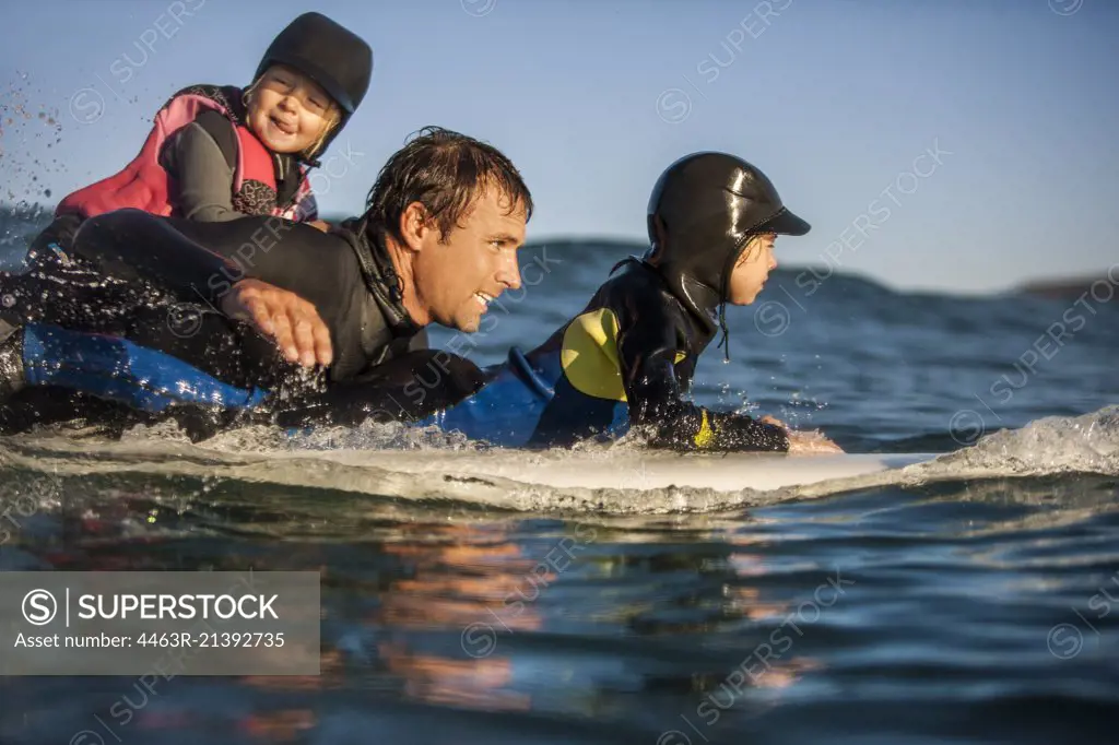 Middle aged man surfing with his two young daughters.