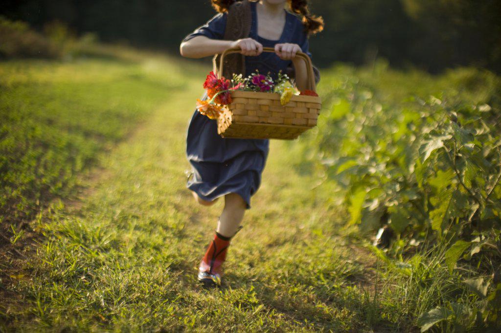 Basket of flowers being held by a young girl running through a field.