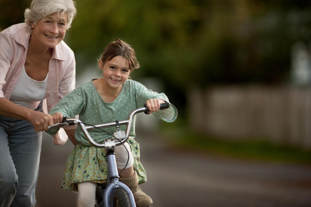 Little girl learning to ride her bicycle with the help of her grandmother.