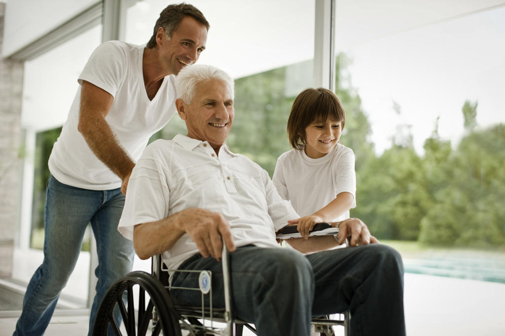 Senior man being pushed in wheelchair,  by his adult son and his grandson.