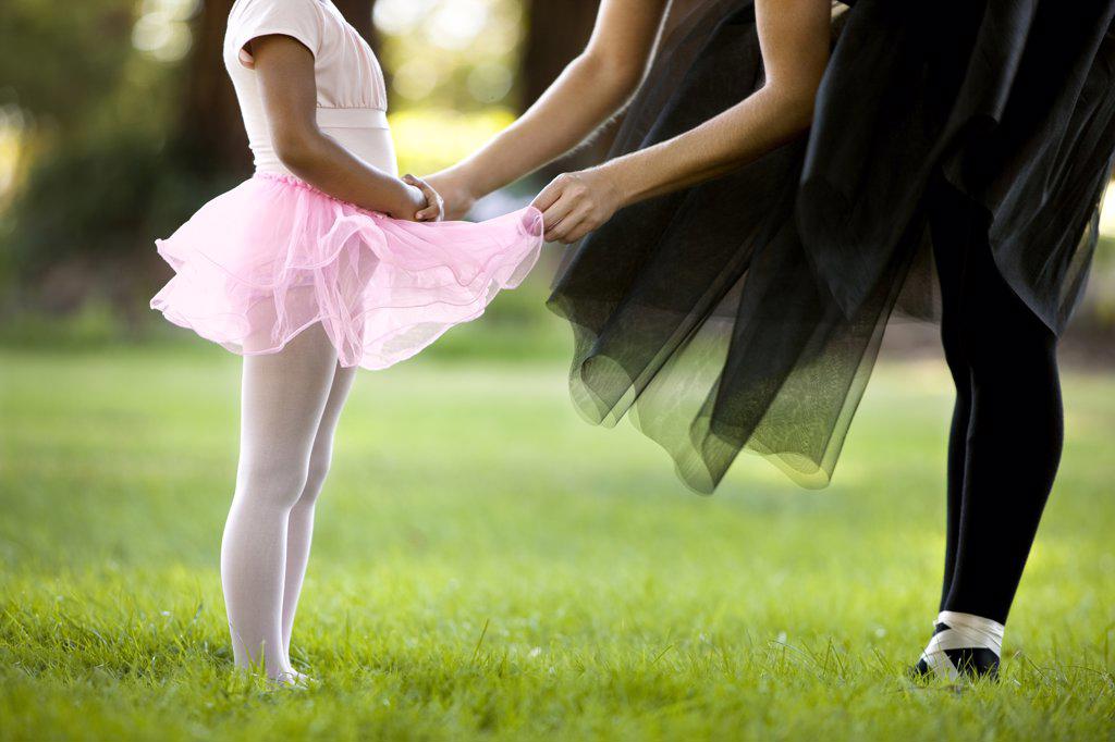 Mid adult woman and her young daughter ballet dancing in a park.