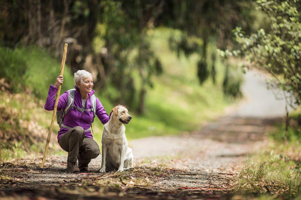 Portrait of a cheerful mature woman taking a break from hiking in the forest to pet her dog.