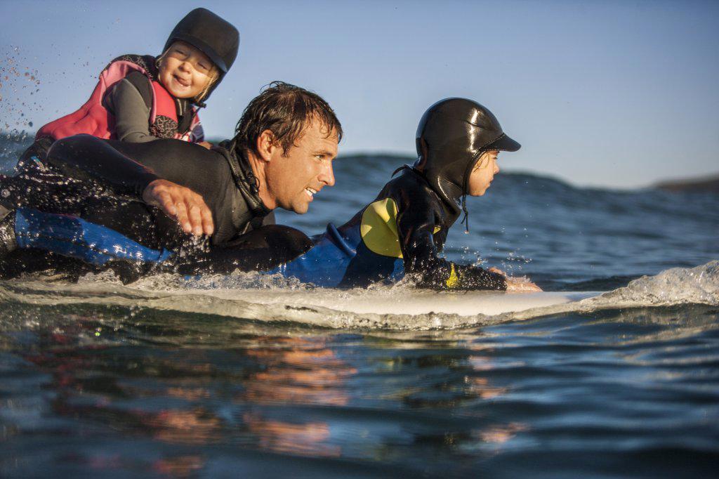 Middle aged man surfing with his two young daughters.
