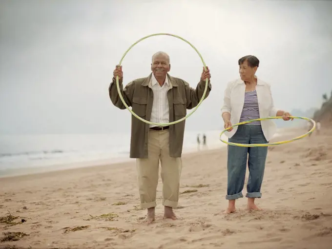 Mature adult couple playing with hula-hoops on a beach.