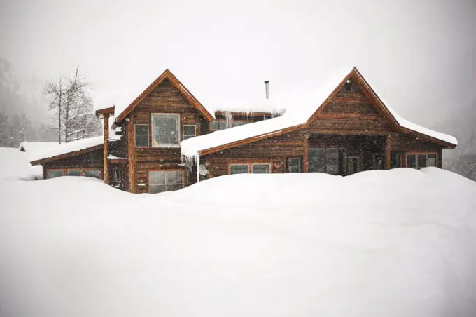 Log cabin covered in snow during a snow storm.