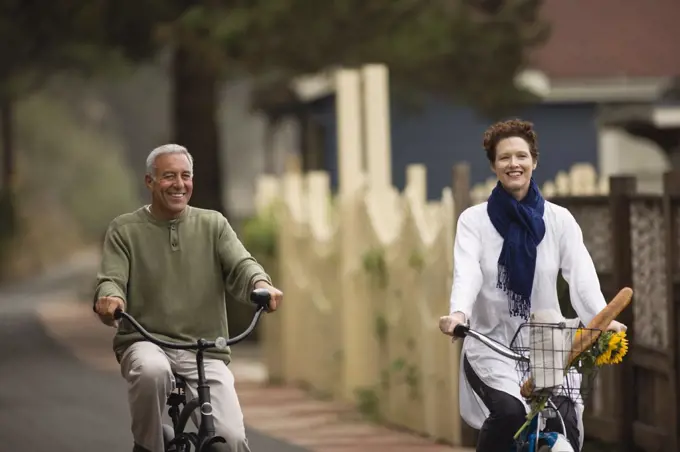 Mature man and a young woman having fun while riding bicycles through a suburban neighborhood.