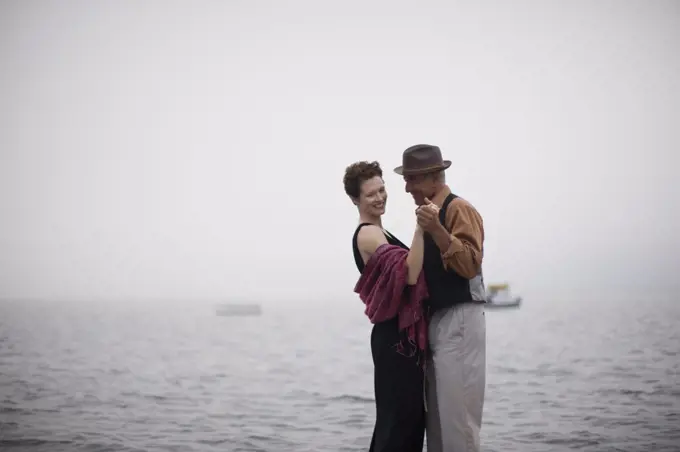 Smiling couple dancing near the open sea on a misty day.