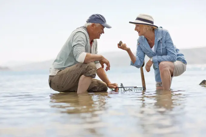 Smiling senior couple collecting rocks on a beach at low tide.